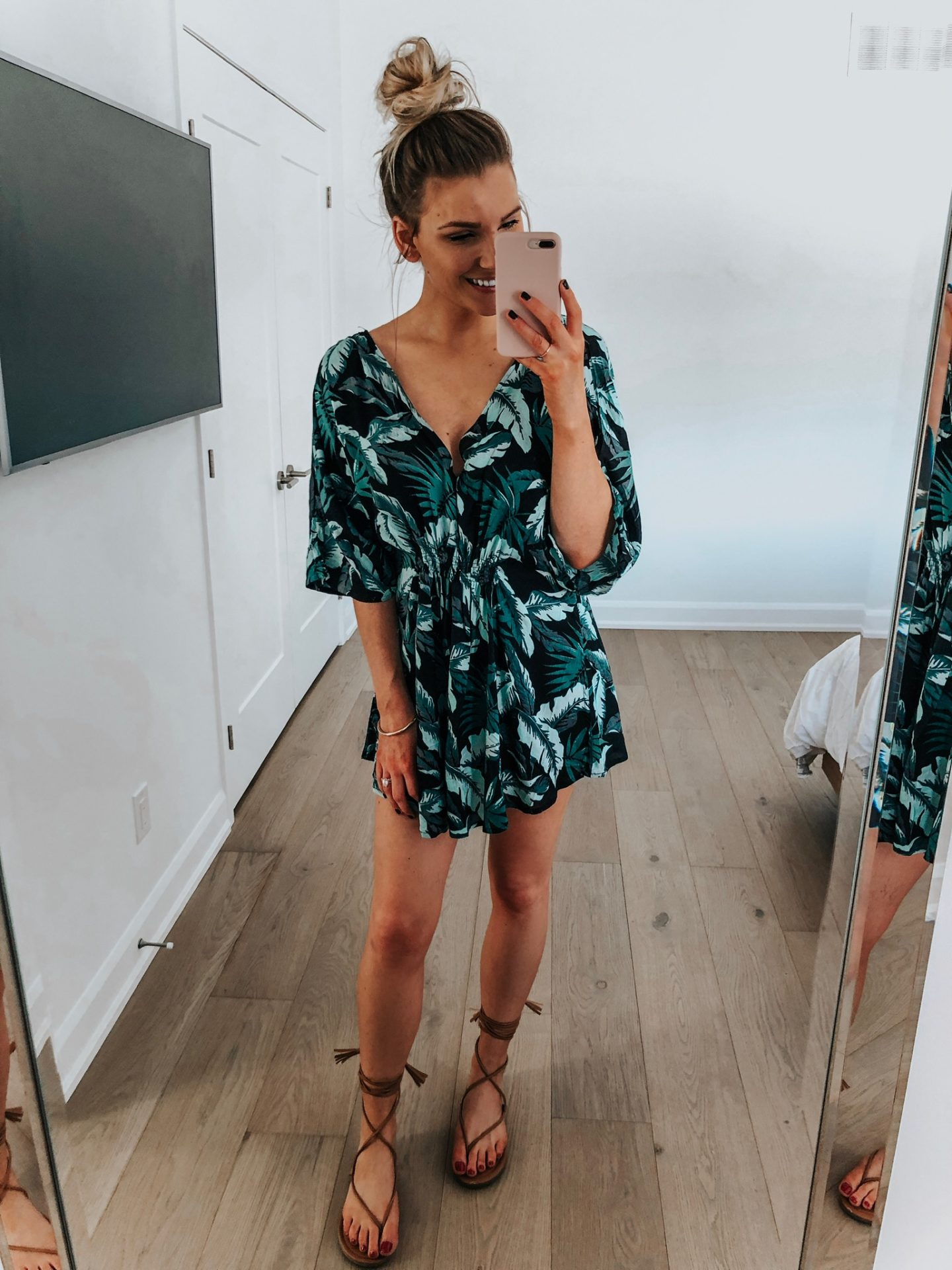 fashion blogger taking selfie in mirror wearing palm printed swimsuit cover up with tan gladiator sandals