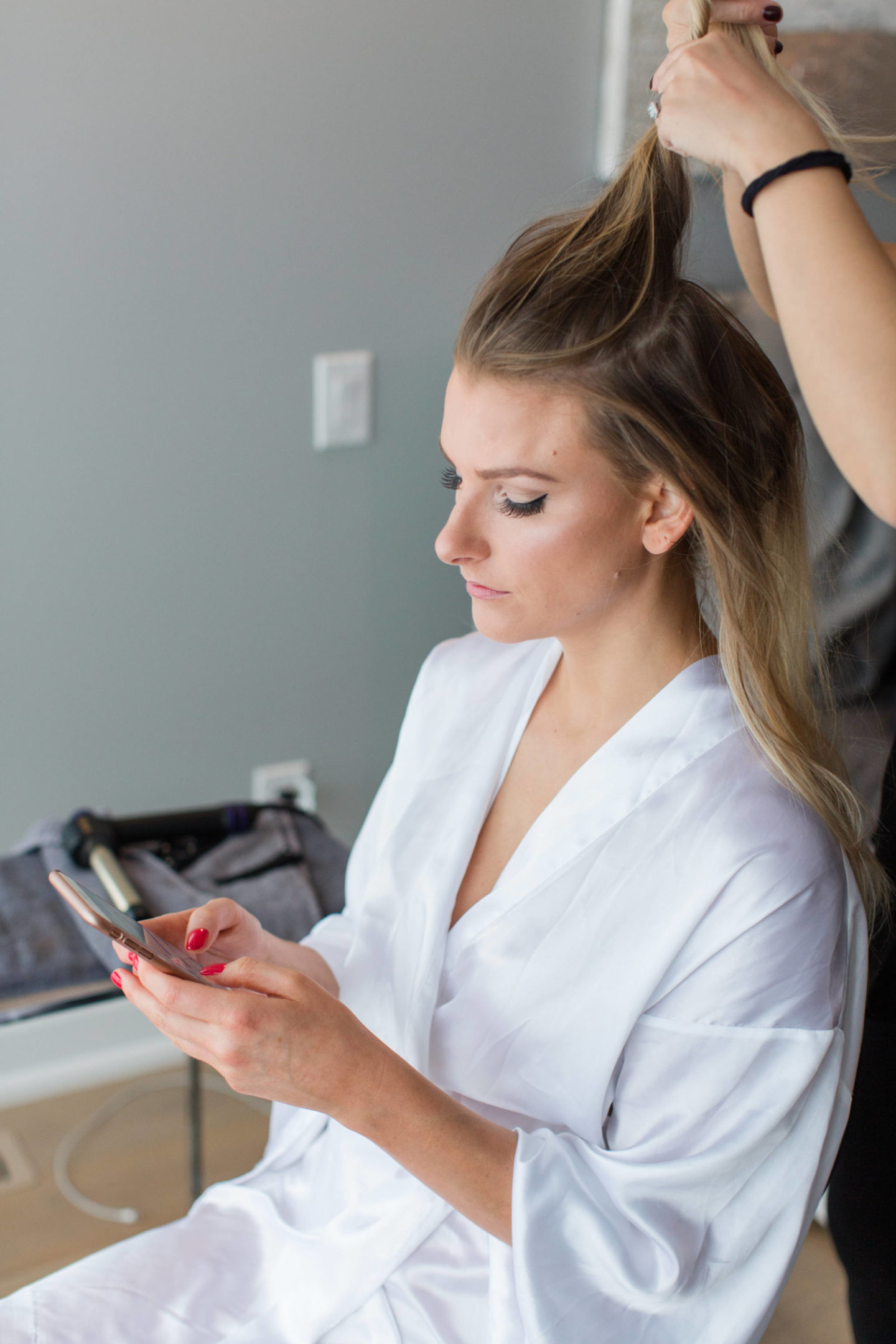 bride getting hair done while working on phone